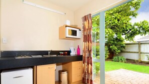 Cozinha compacta com micro-ondas, pia e armários, que dá para um pátio com porta de vidro e vista para um jardim verde.