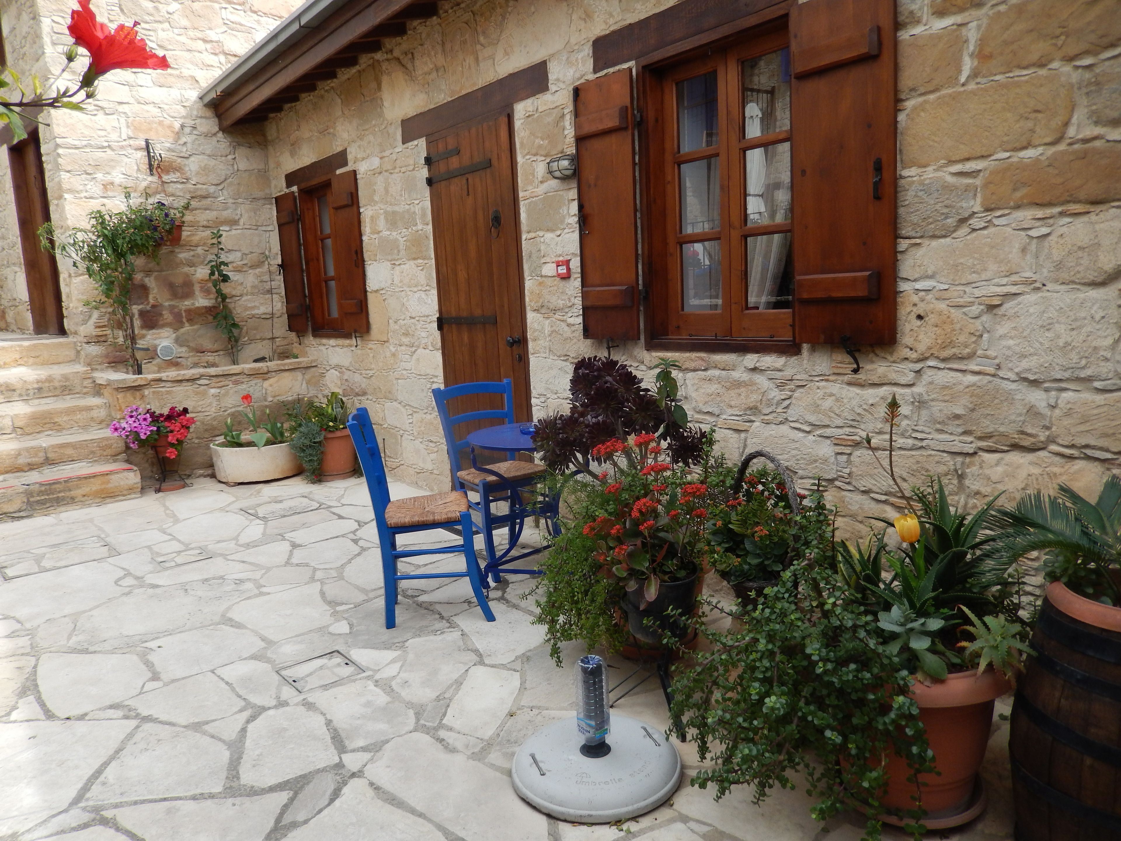 A stone building with wooden shutters, a blue chair, and potted plants.