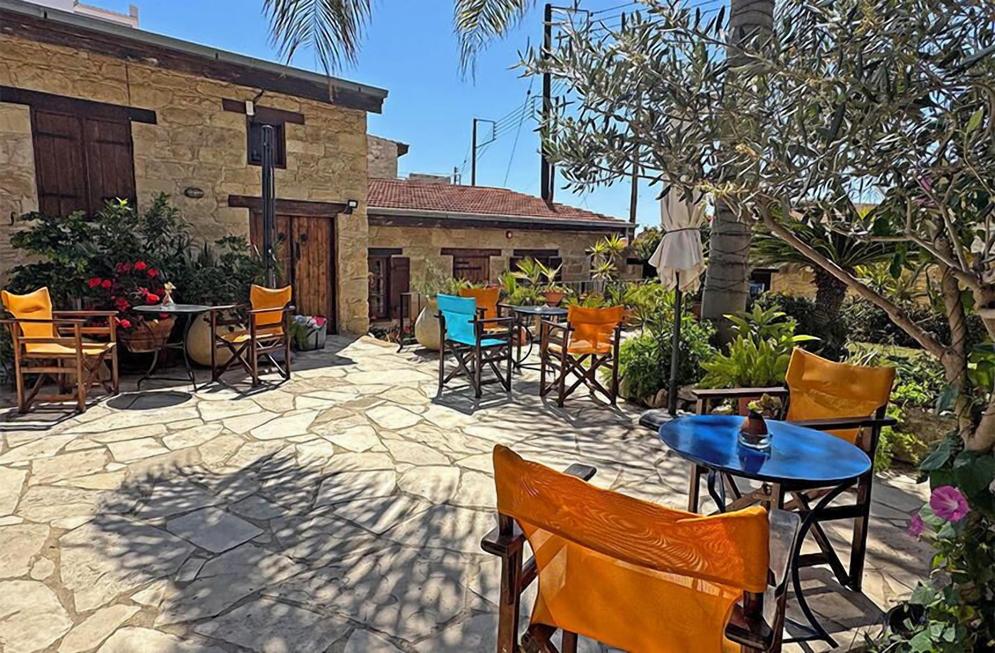 Un espace extérieur aménagé en terrasse, avec un sol en pierre, plusieurs tables et chaises, et des plantes en pot.