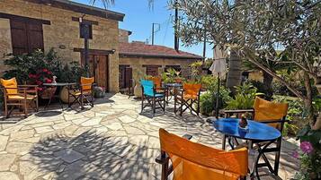 An outdoor patio area with stone flooring, multiple tables and chairs, and potted plants.