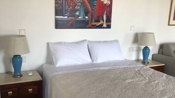 A hotel room with a large bed, two nightstands with lamps, a painting on the wall, and a gray armchair.