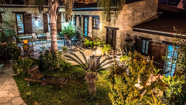 A stone building with a patio area featuring outdoor seating and lush greenery. - Nikis House (Limassol)