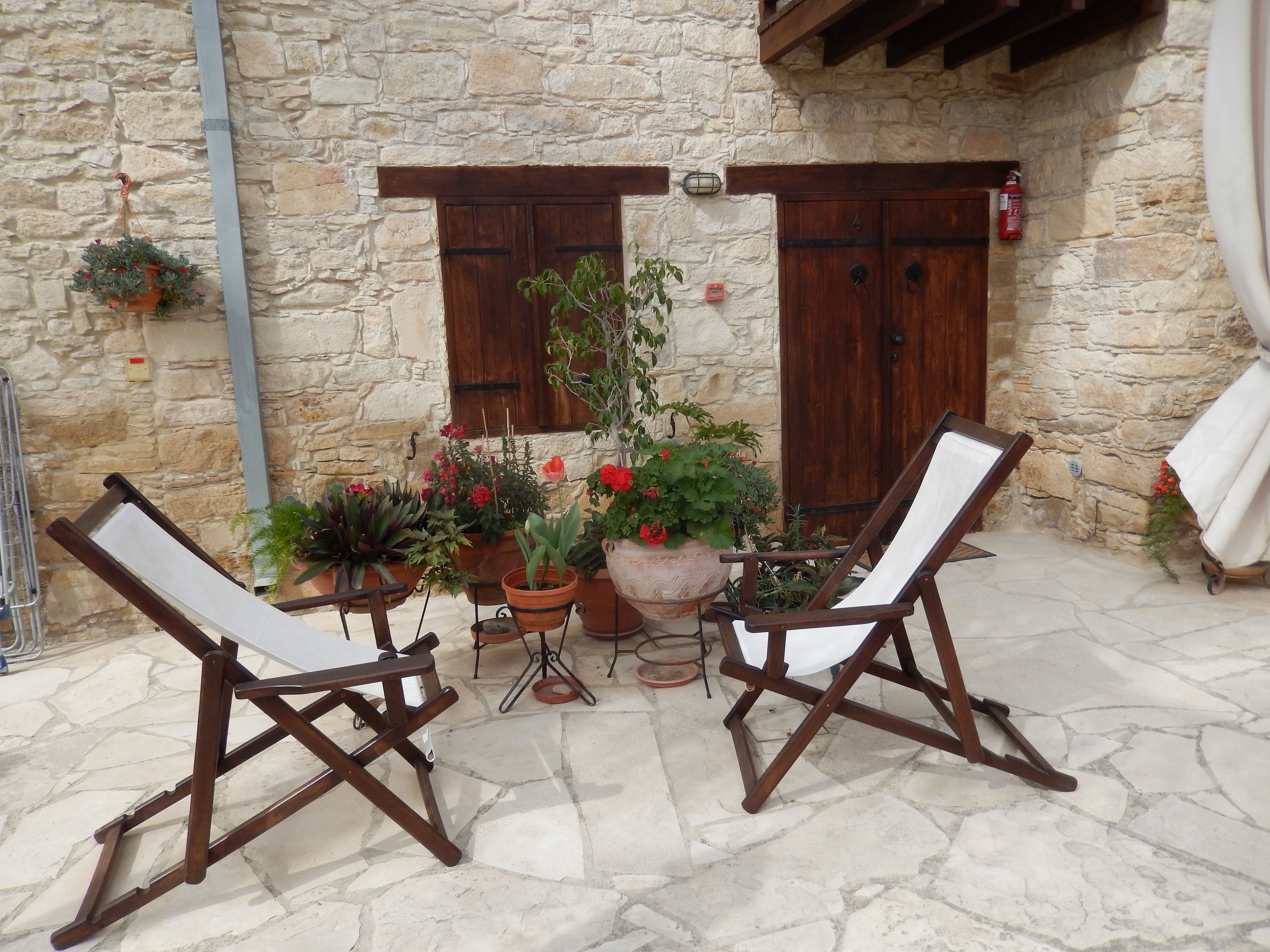 A stone-walled patio with two wooden chairs, potted plants, and a table.