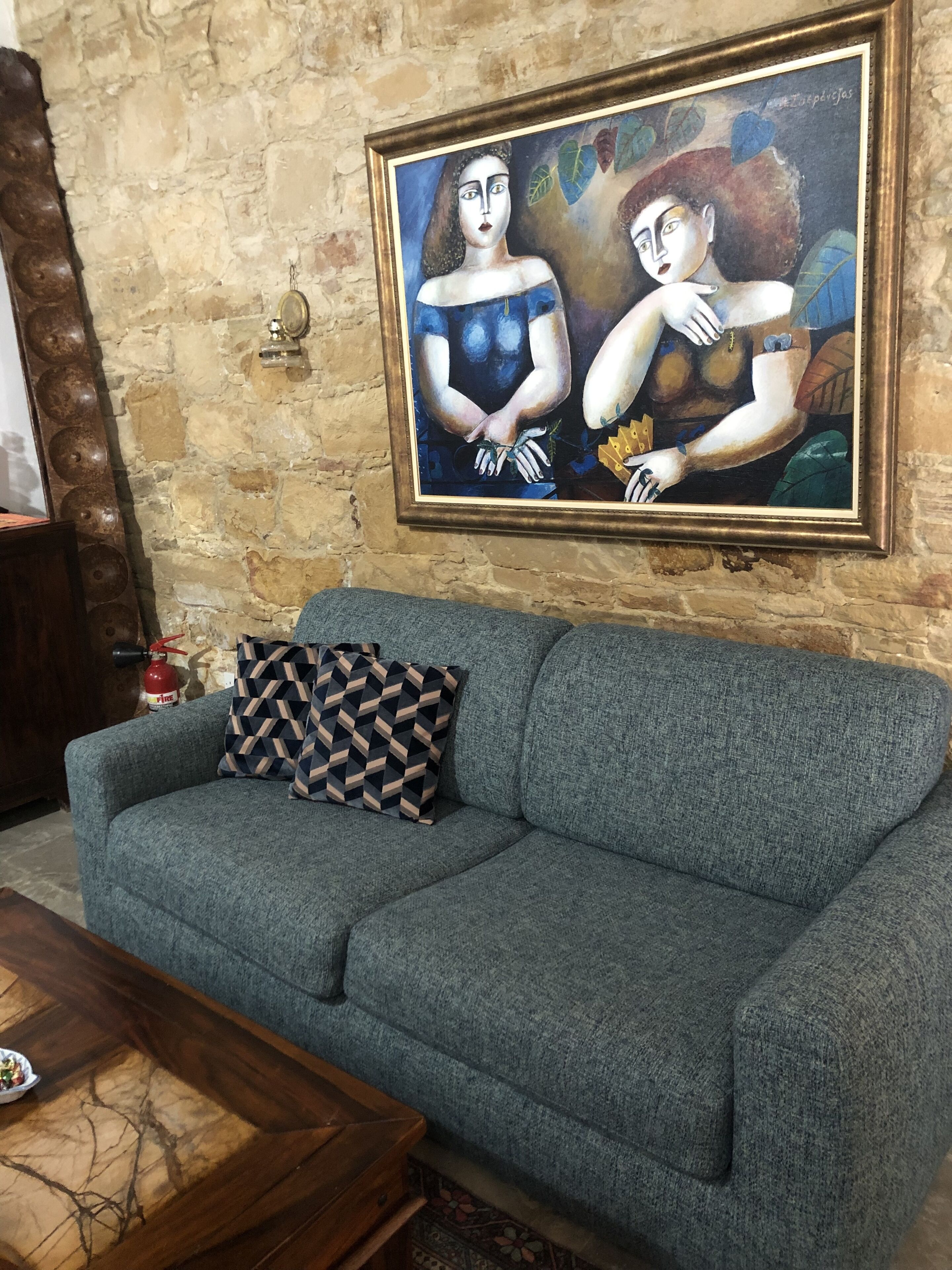 A living room with a stone wall, a blue sofa, a patterned throw pillow, and a framed painting.
