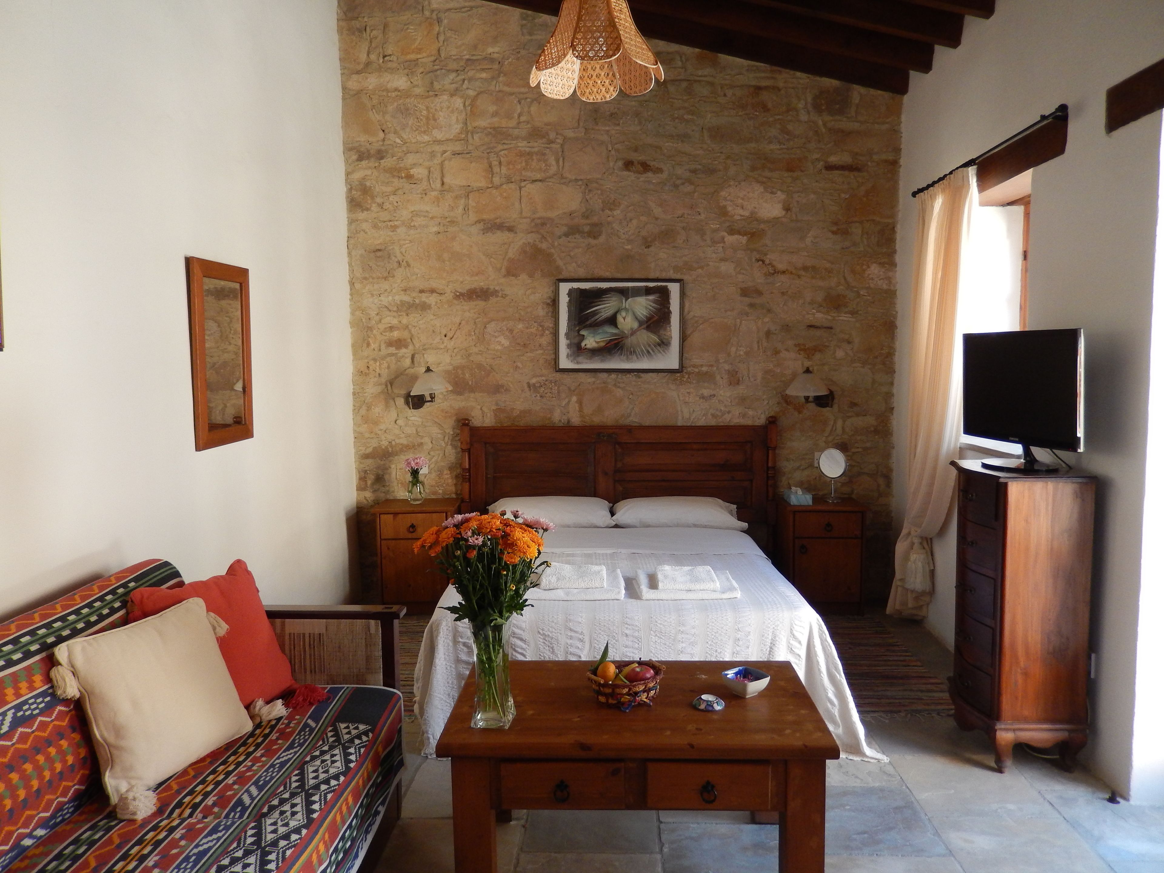 Un dormitorio acogedor con pared de piedra, una cama de madera, un televisor y una mesa con flores y fruta.