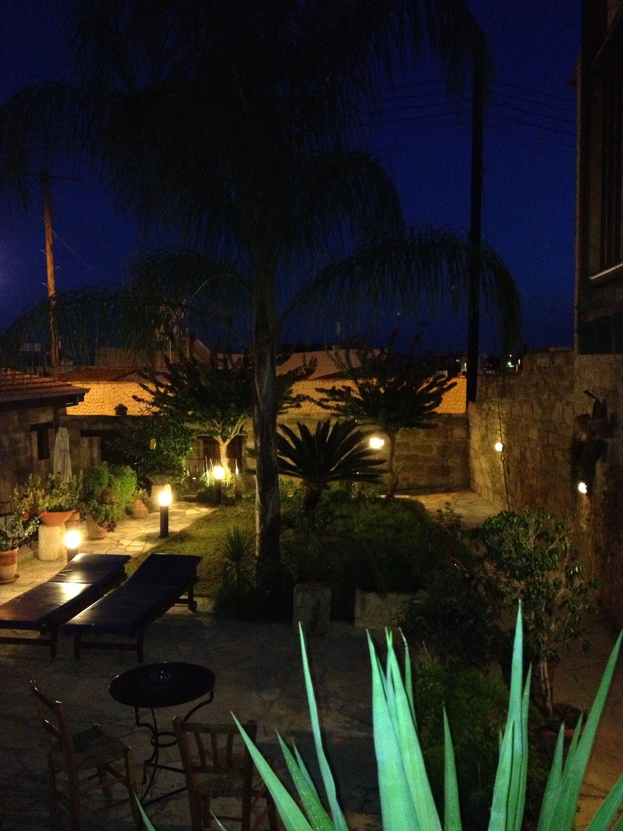 Eine Terrasse im Freien bei Nacht mit Steinmauern, Palmen und Topfpflanzen.