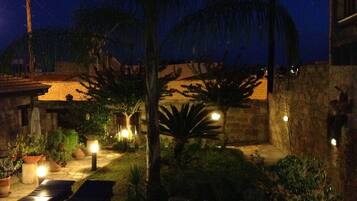 Eine Terrasse im Freien bei Nacht mit Steinmauern, Palmen und Topfpflanzen.