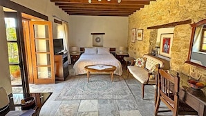 A bedroom with a bed, bedside tables, a wooden chair, a sofa, a stone wall, and a stone floor. - Nikis House (Limassol)