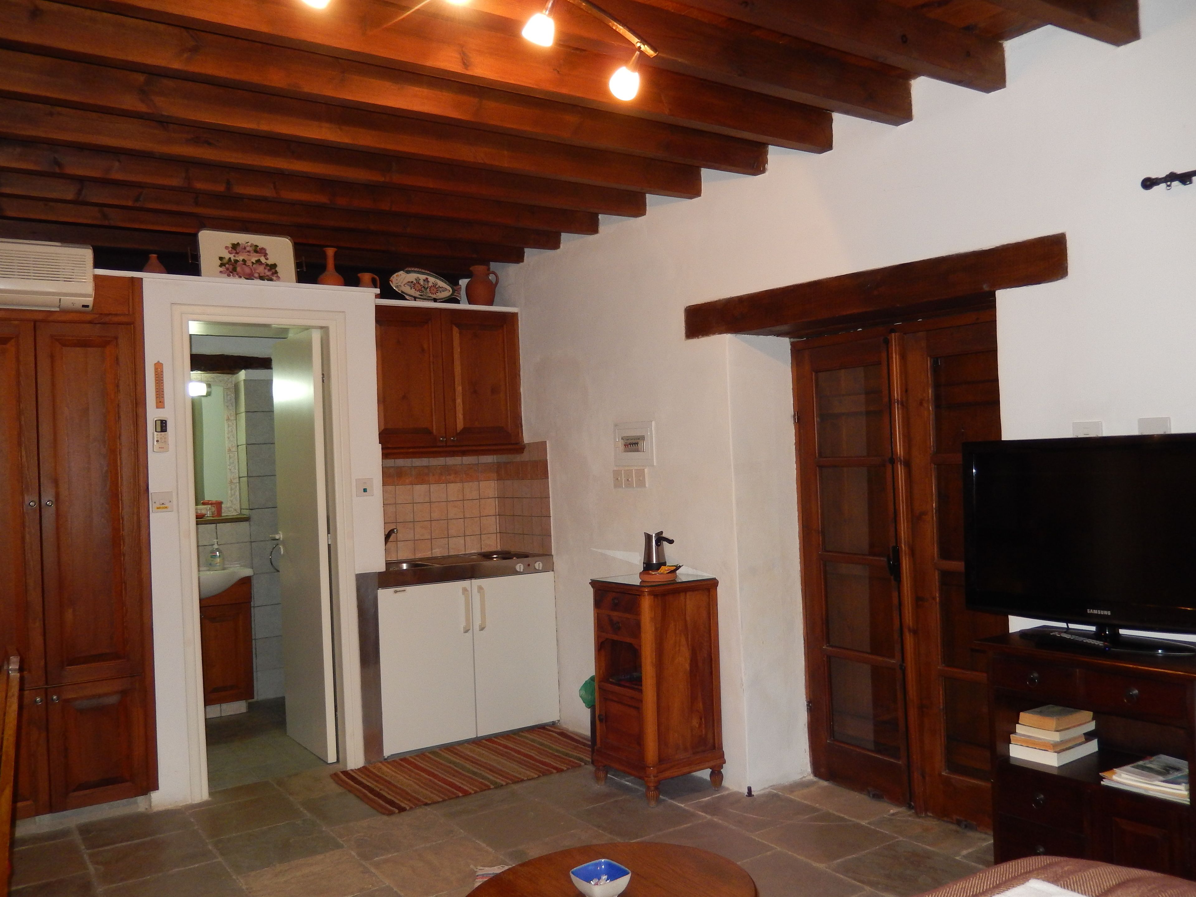 A compact kitchen with wooden cabinets, a stove, and a television on a wooden stand.