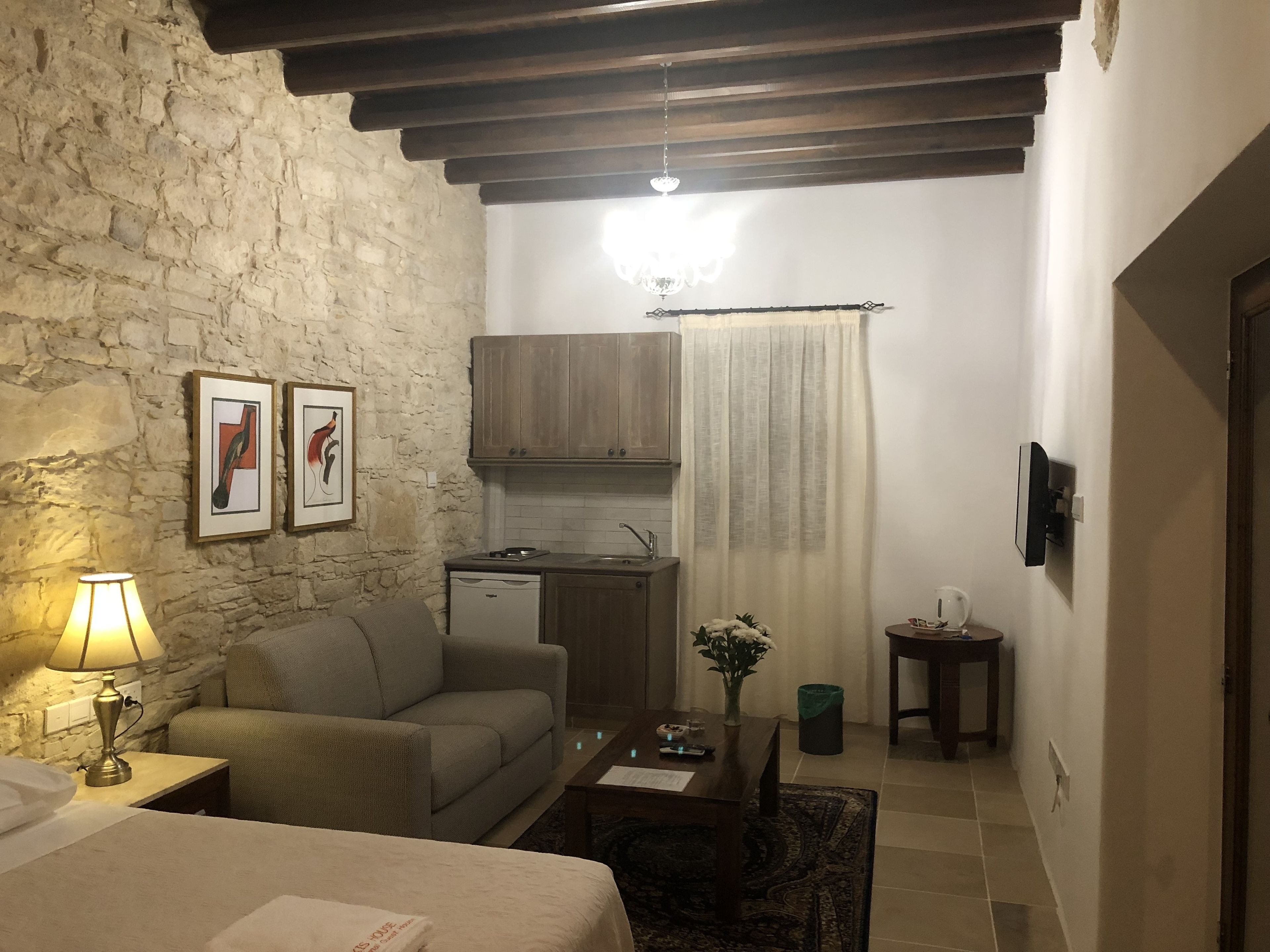 Une chambre d’hôtel compacte avec un mur en pierre, une kitchenette, un canapé, une petite table et un lit.