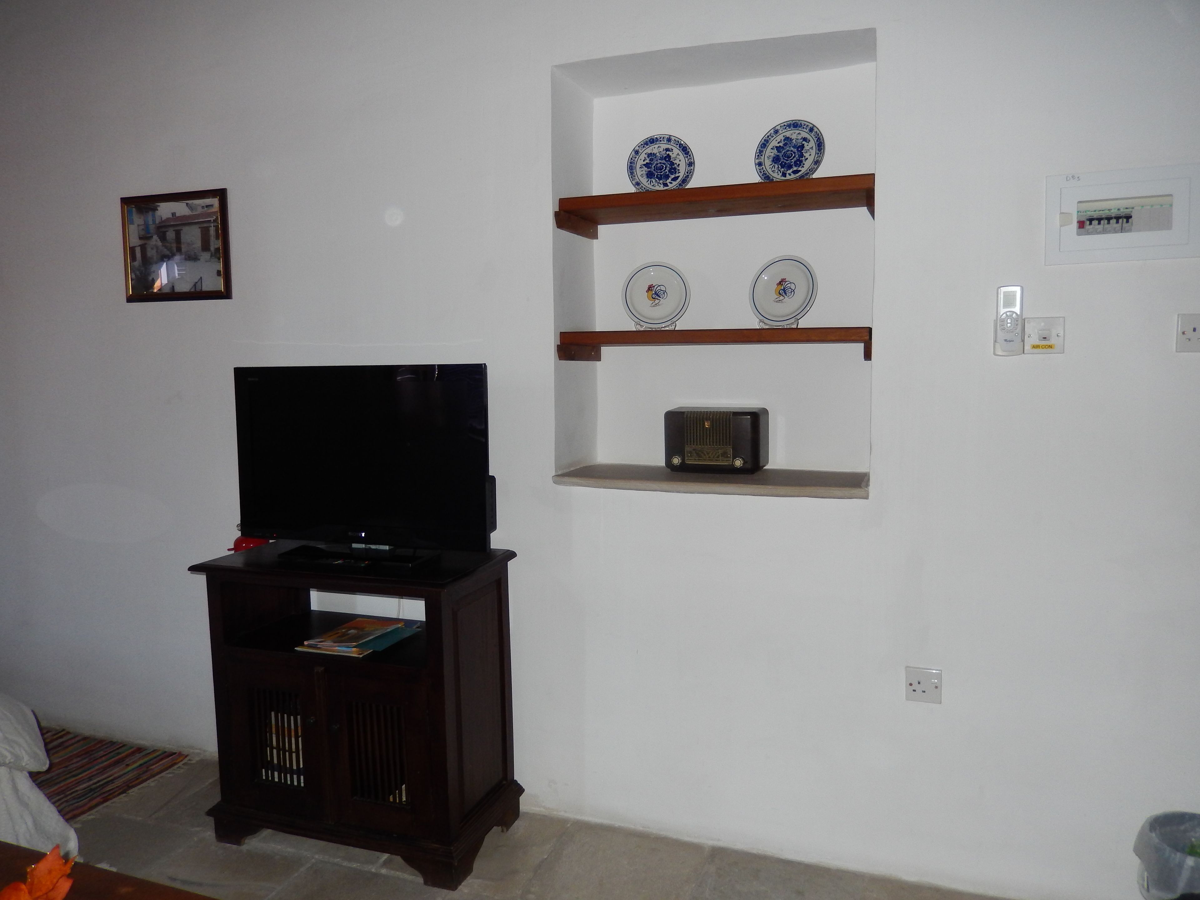 Una sala de estar con un televisor sobre un mueble de madera, un estante con platos decorativos y un aire acondicionado instalado en la pared.