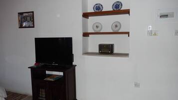 Una sala de estar con un televisor sobre un mueble de madera, un estante con platos decorativos y un aire acondicionado instalado en la pared.