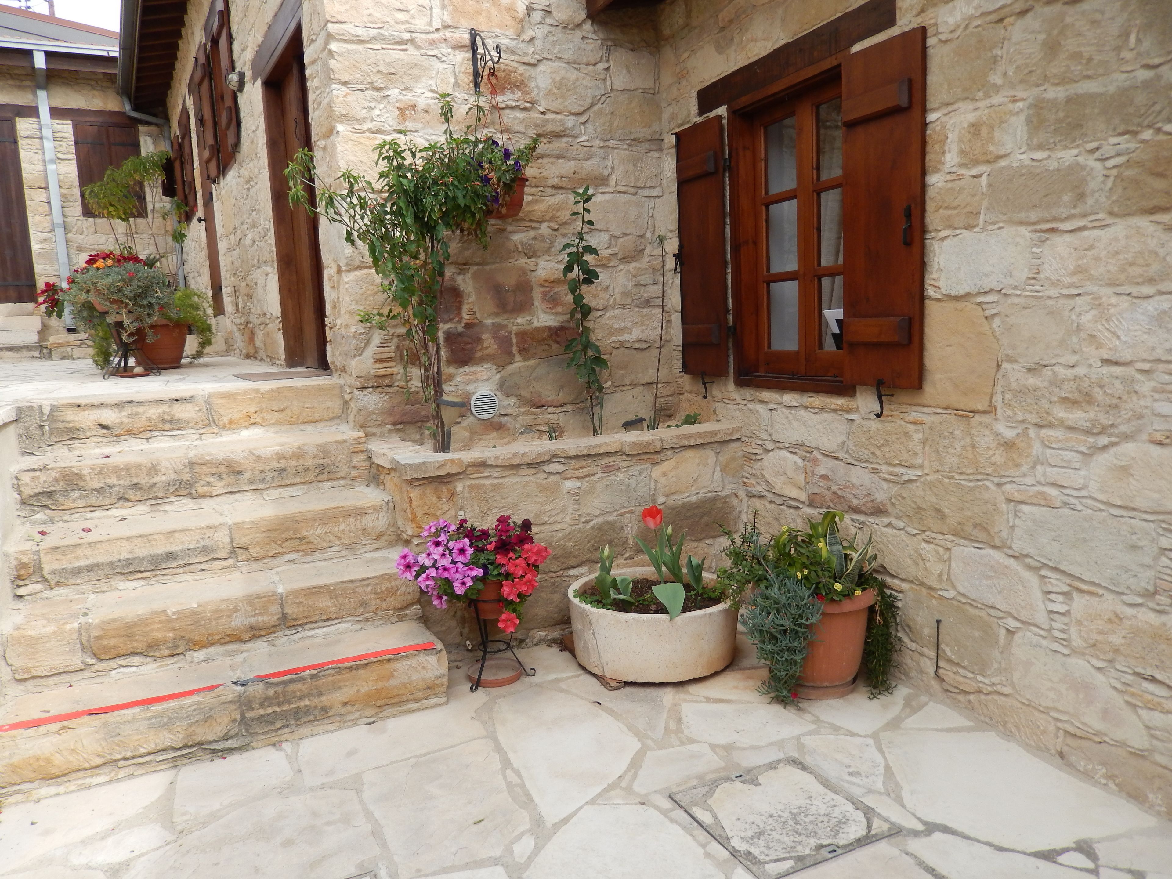 A stone building with wooden shutters, a stone staircase, and potted plants.