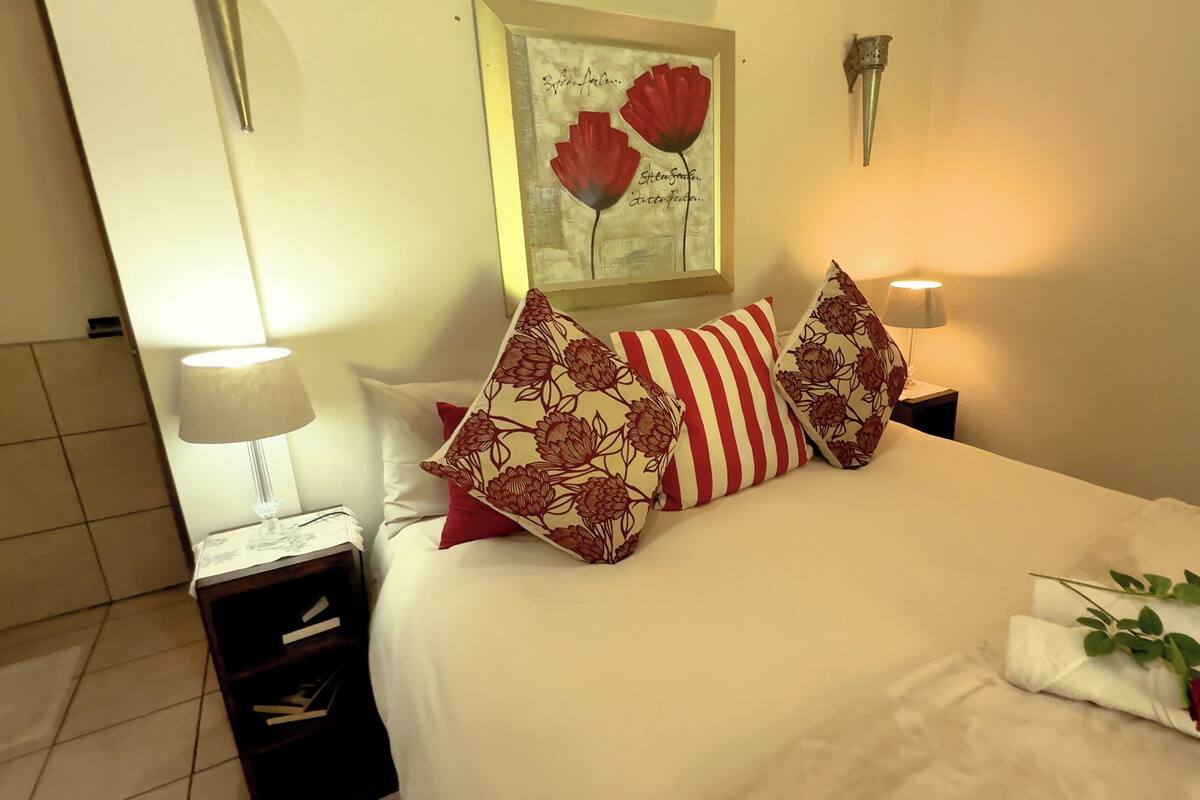 A neatly made bed with floral pillows, a bedside lamp, and a framed artwork above it.