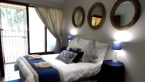 A bedroom with a bed, two bedside lamps, a window with curtains, and two wall mirrors. - A Cherry Lane Self Catering and B&B (Bloemfontein)