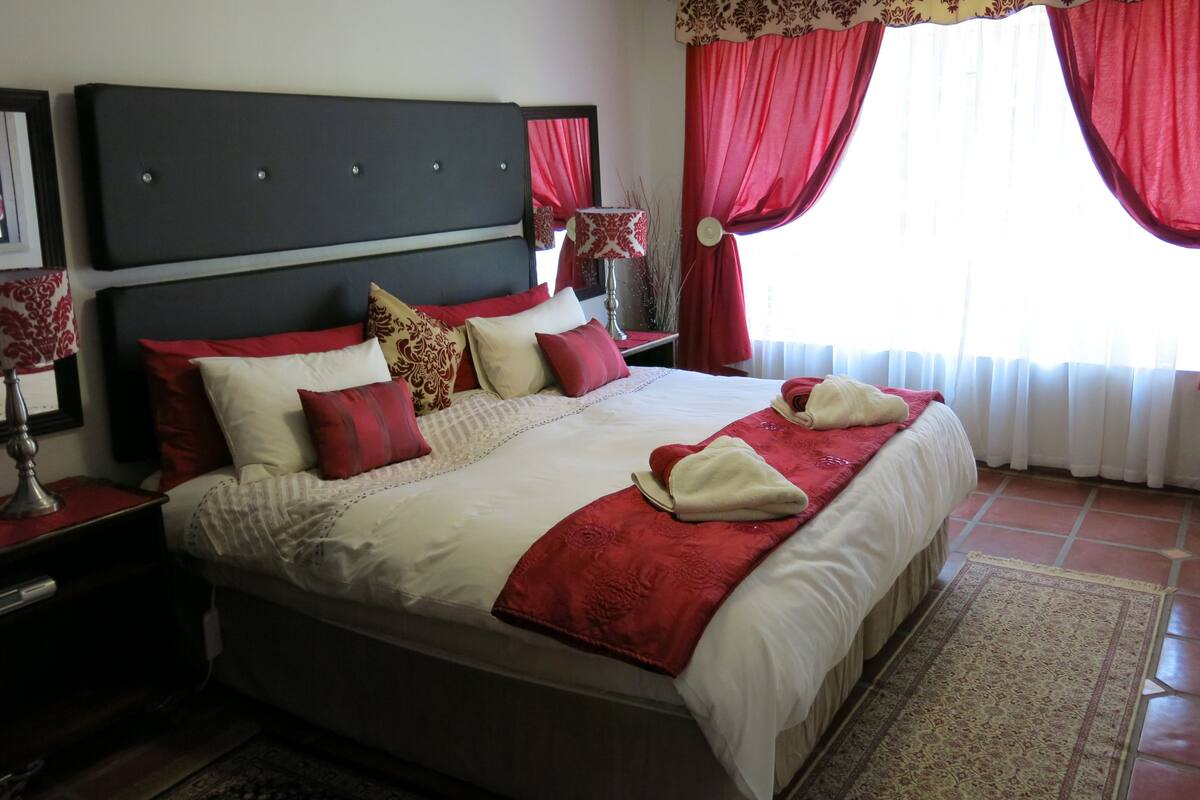 A neatly made bed with red and white bedding, a dark headboard, and a red and white patterned area rug.