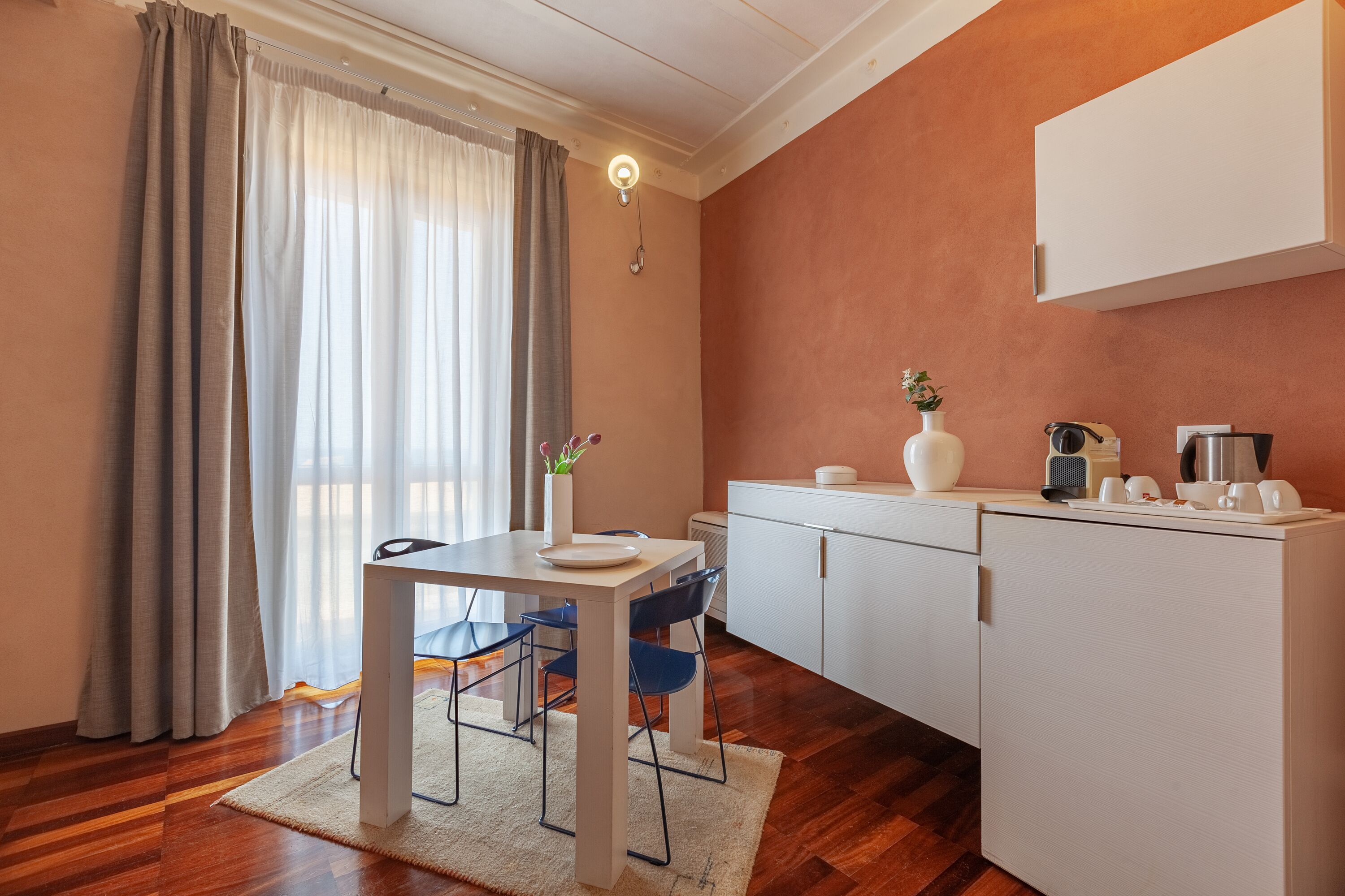 A compact kitchen with a dining area, featuring a table, chairs, a cabinet, and a countertop with kitchen appliances.