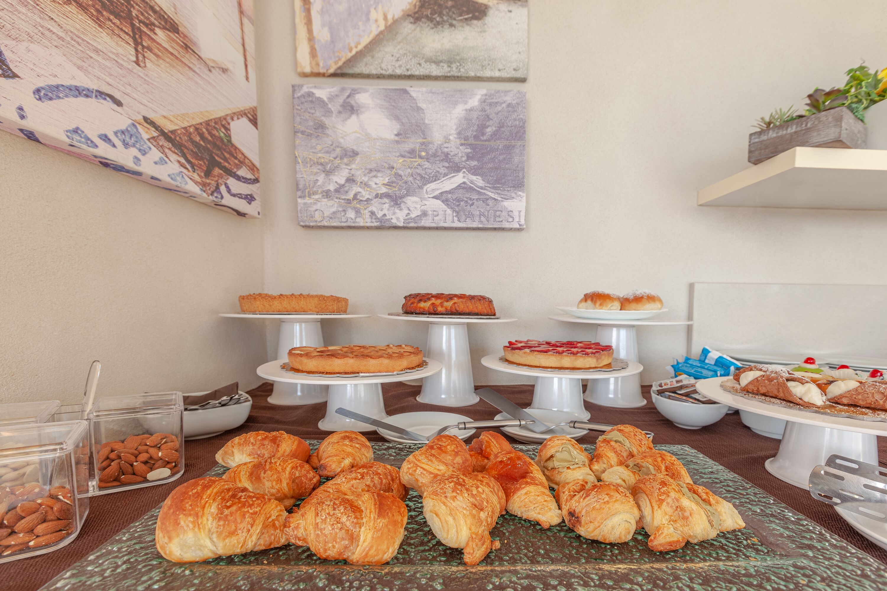 Um buffet de café da manhã com pães, croissants e uma variedade de sobremesas à mostra.