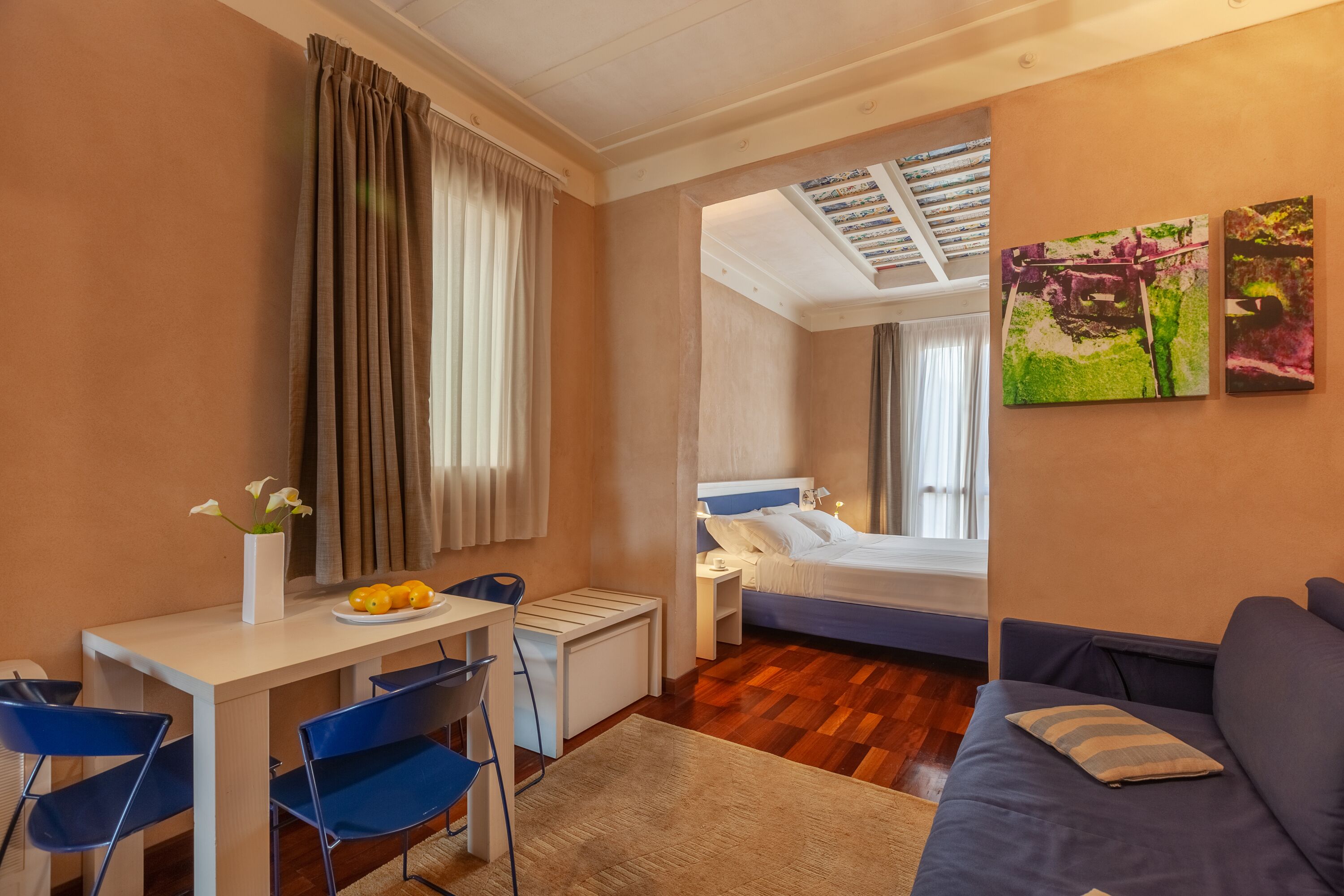 A hotel room with a bed, a desk with a chair, a small table with a plate of fruit, and a sofa.