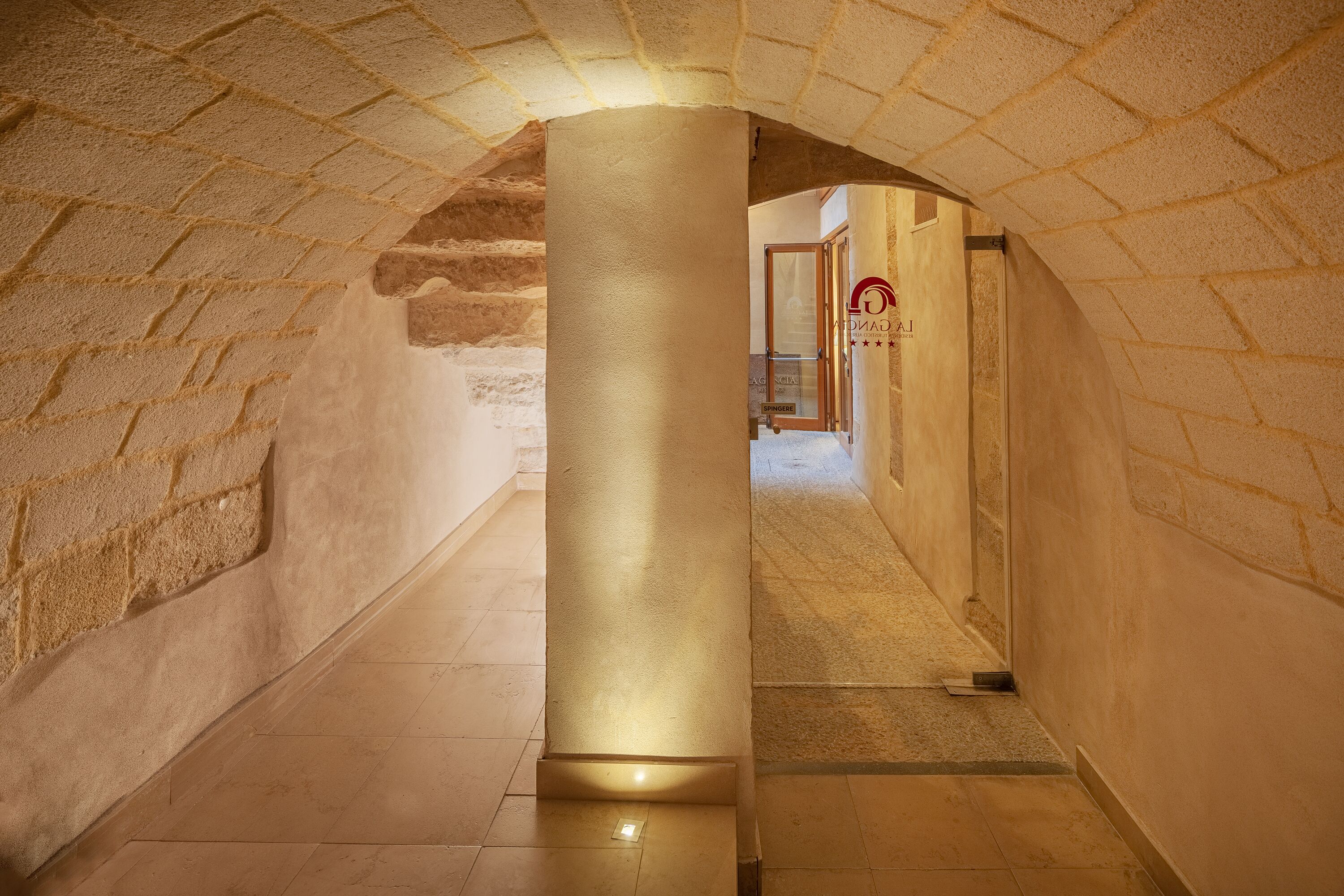 A stone-walled hallway with a central column and a door at the end.