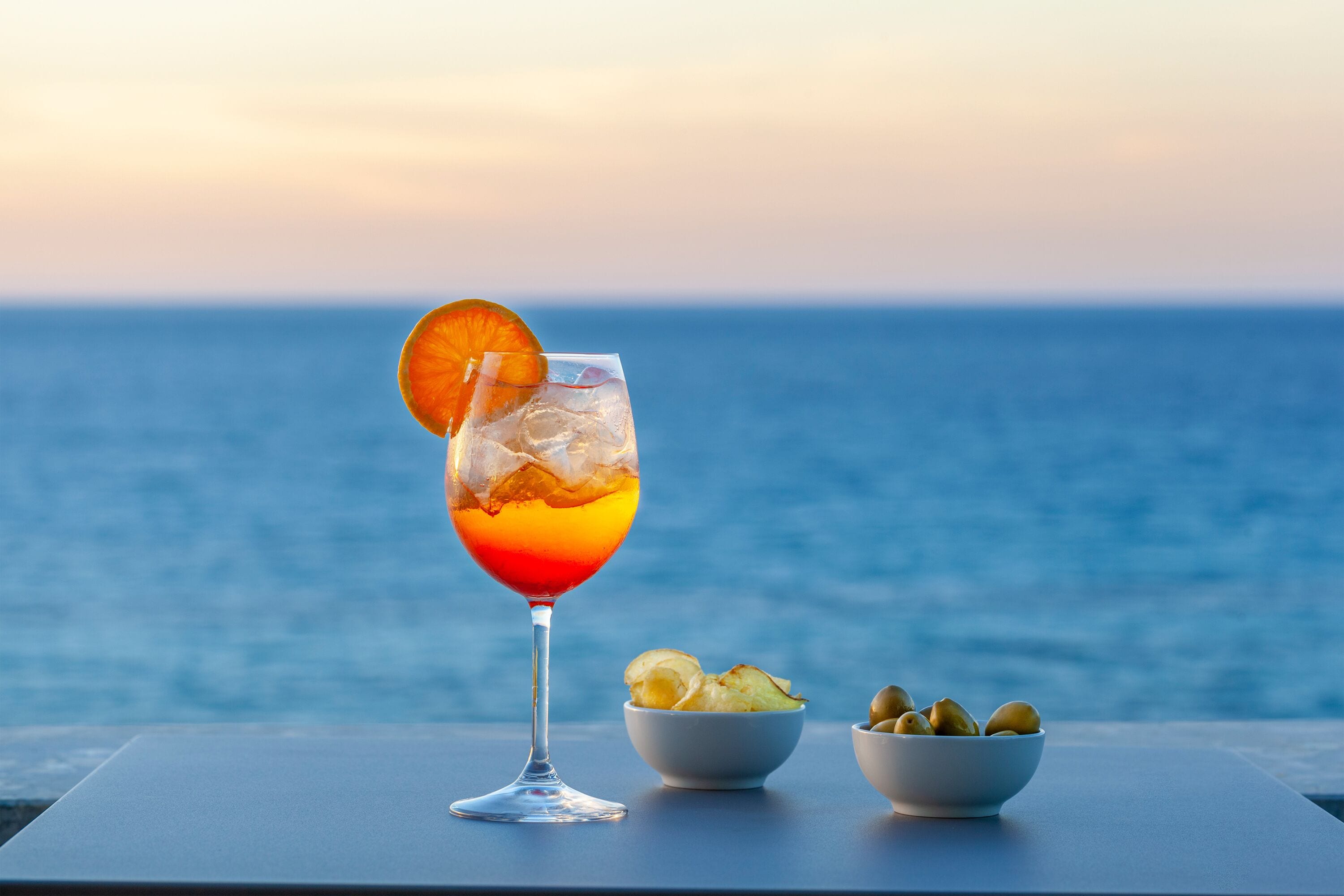 Ett glas med en drink och en apelsinskiva på ett bord vid havet.