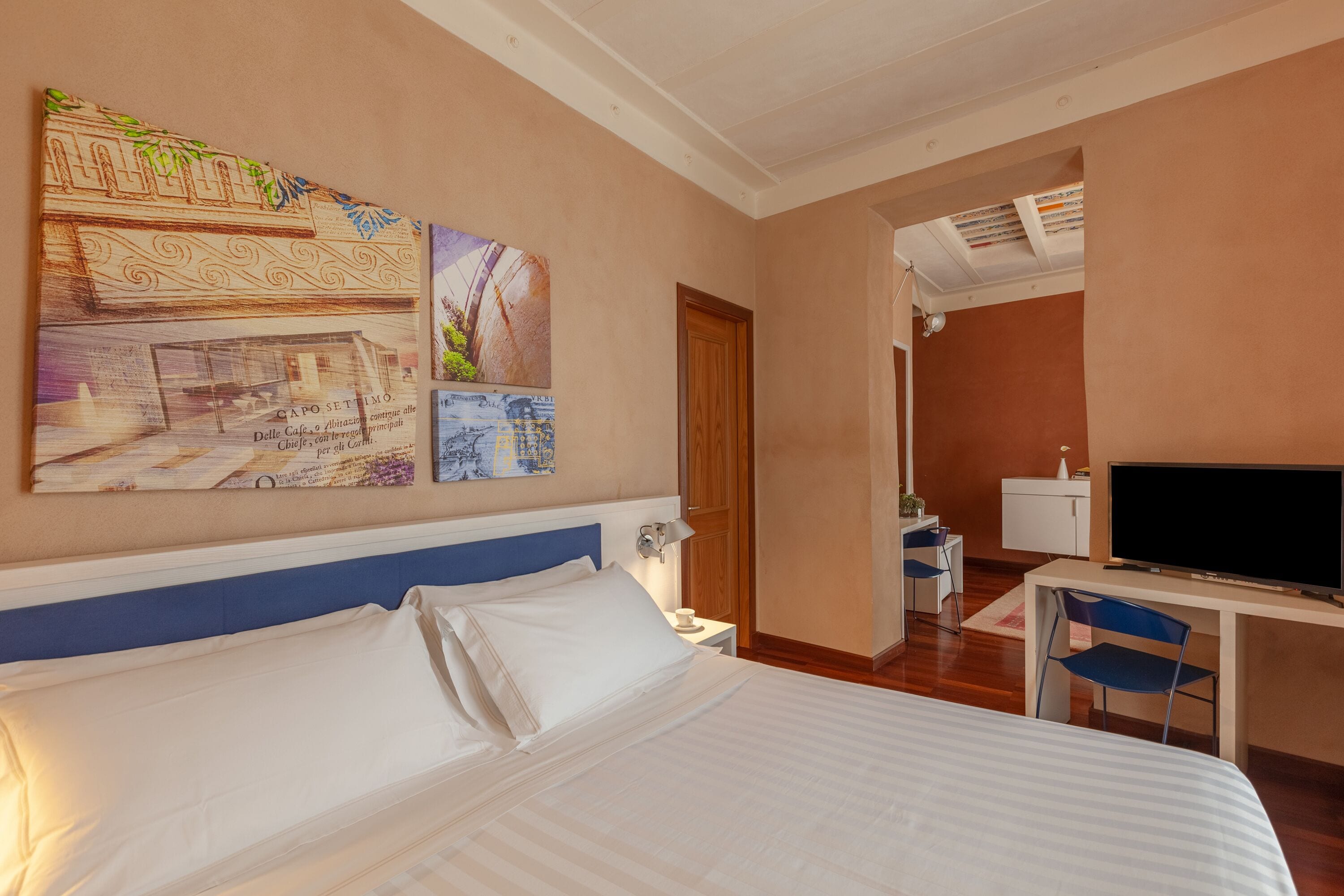 Una habitación de hotel con una cama, un escritorio con televisor y obras de arte en la pared.