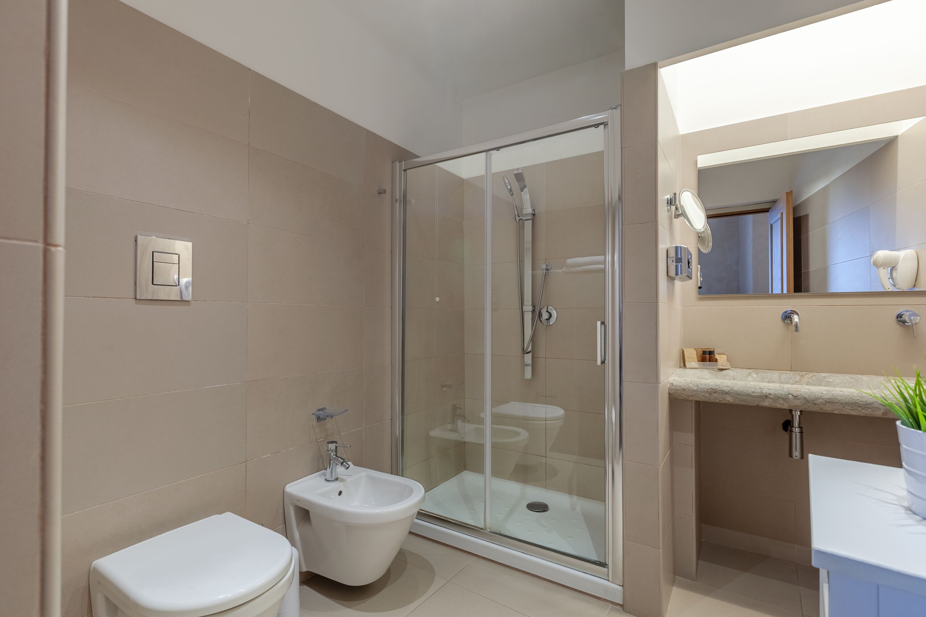 Une salle de bain moderne dotée d’une douche à parois de verre, d’un bidet et d’un lavabo avec un plan de travail en marbre.