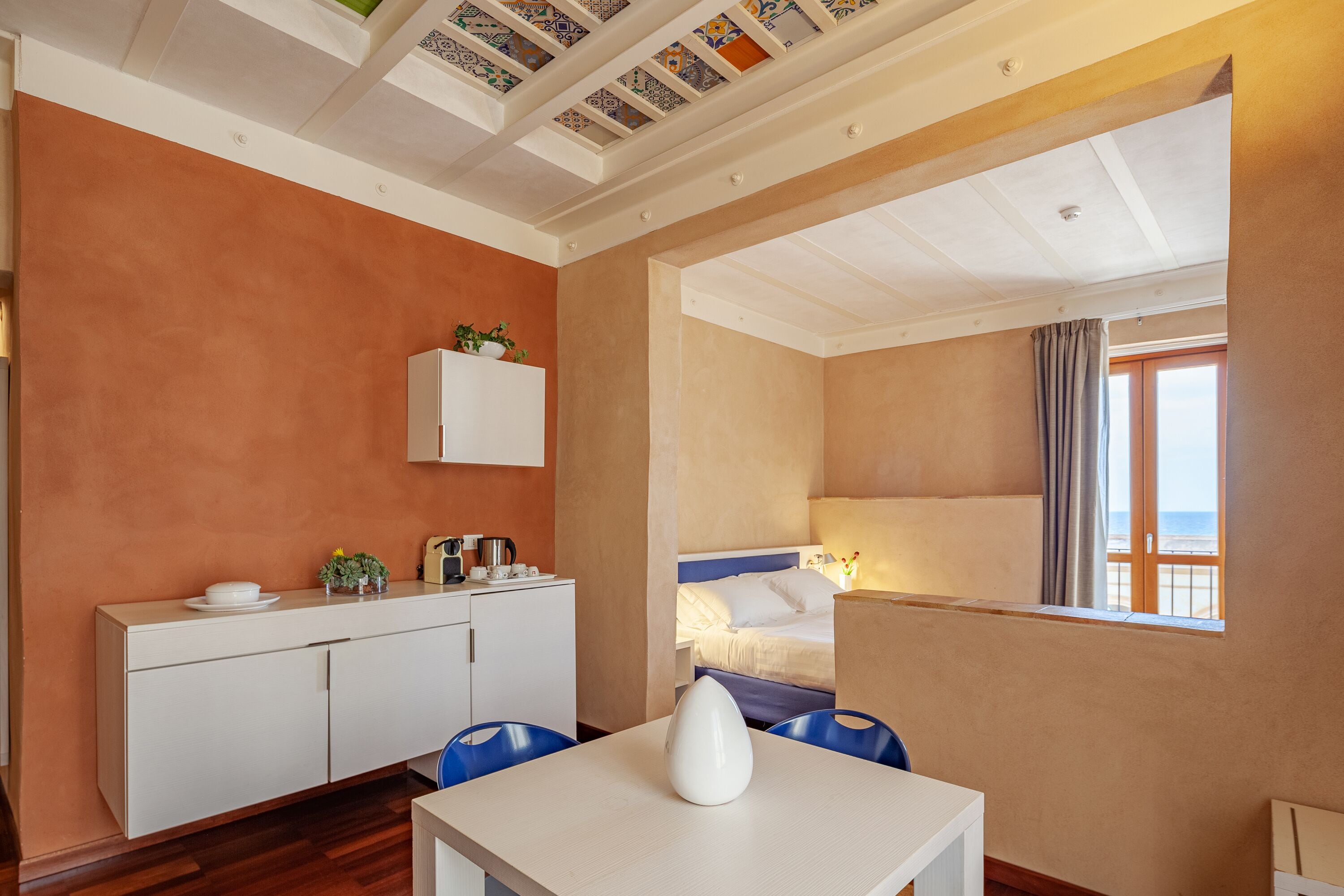 Habitación de hotel con cama, escritorio con silla, kitchenette pequeña y ventana con vista al mar.
