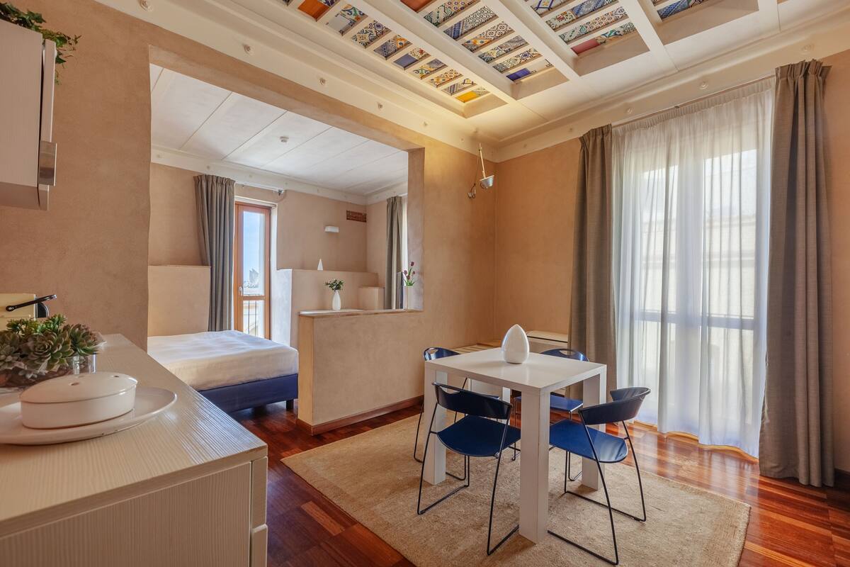 Habitación de hotel moderna con cama, escritorio con sillas, una mesita, lavamanos y un ventanal con cortinas.
