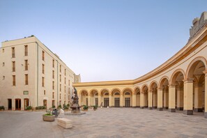 A spacious courtyard with a series of arches and a building with multiple windows and doors.