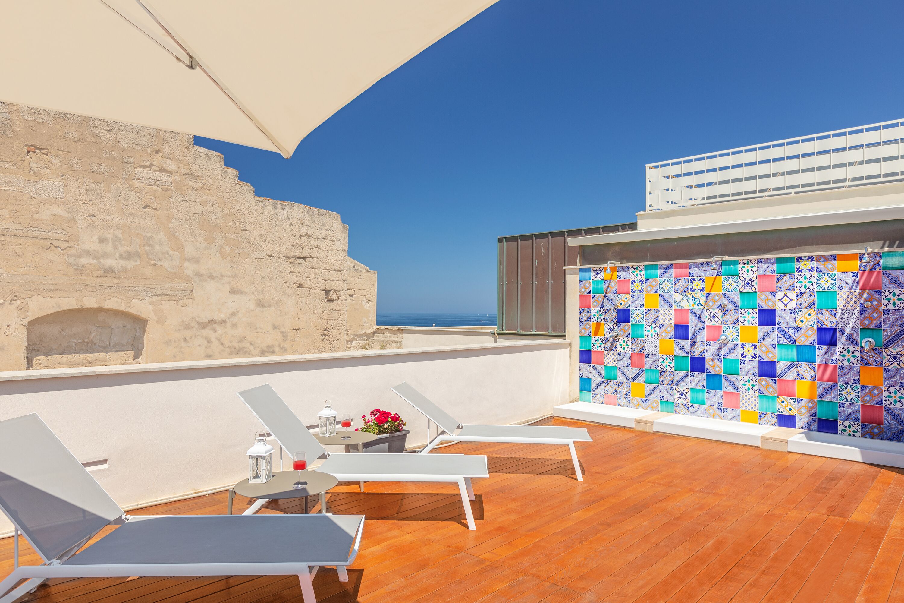 A rooftop terrace with sun loungers, a table with a lantern, and a colorful tiled wall.