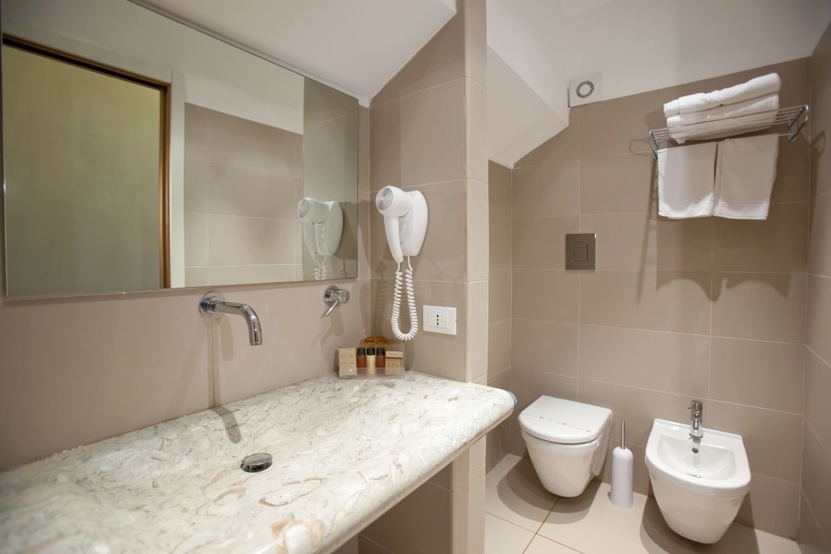 A bathroom with a marble sink, a toilet, a bidet, and a hairdryer mounted on the wall.