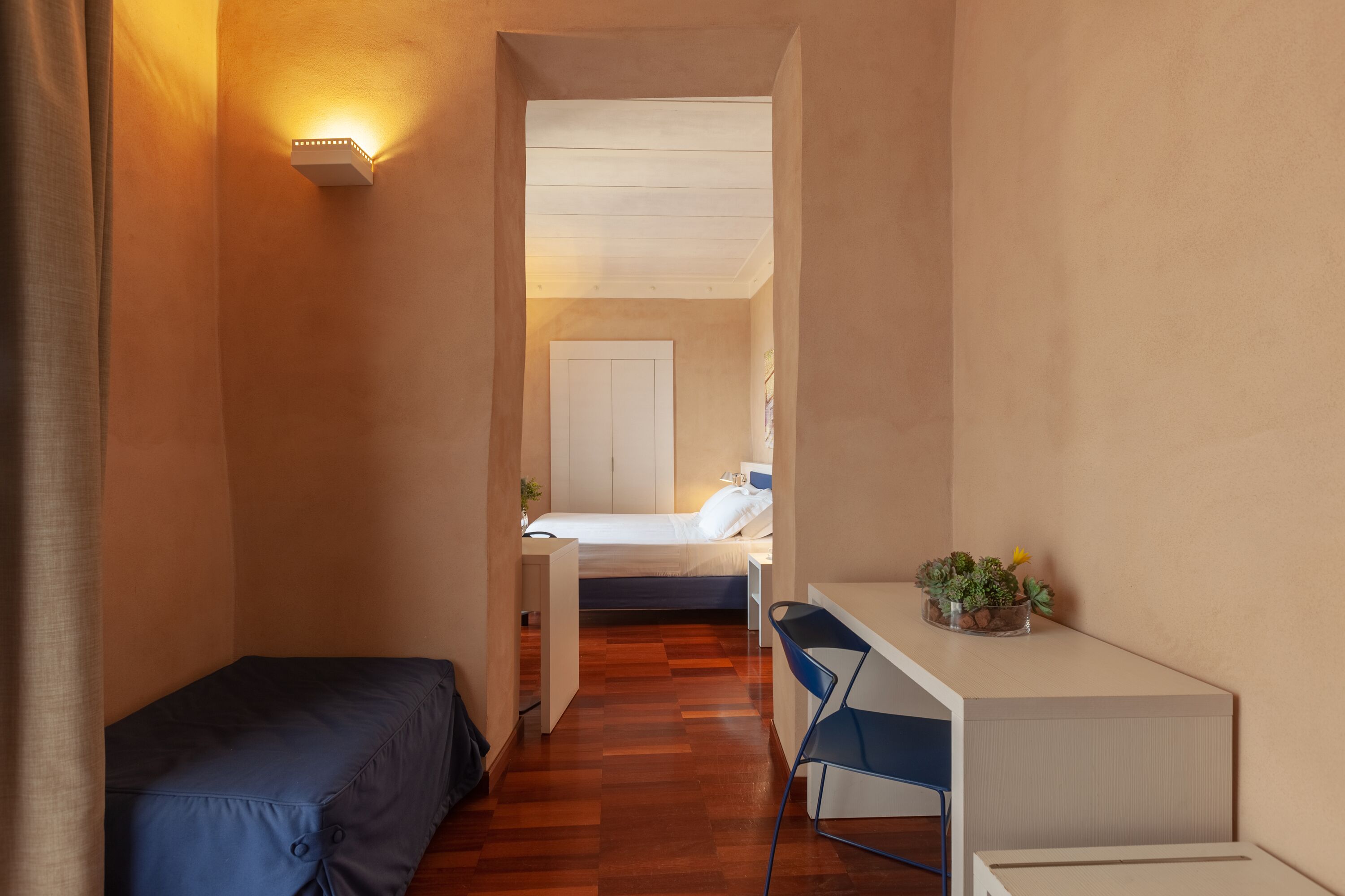 Un corridoio stretto che porta a una camera da letto con un letto, una scrivania e una sedia.