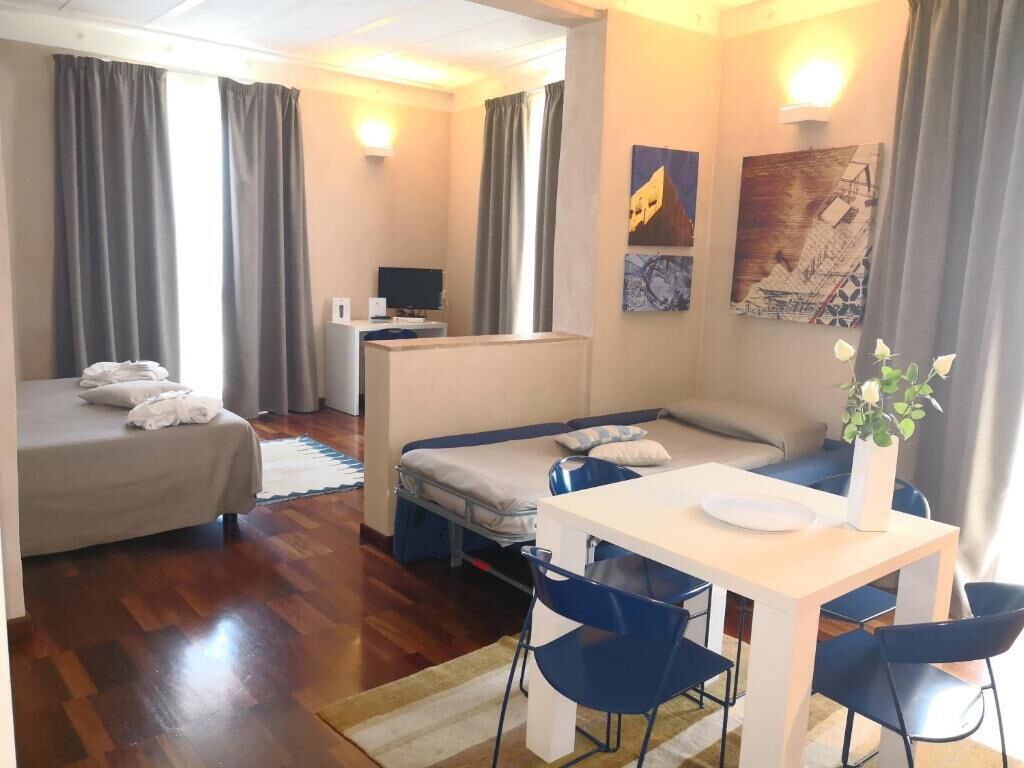 A hotel room with a bed, a sofa, a table with chairs, a desk, and a computer.