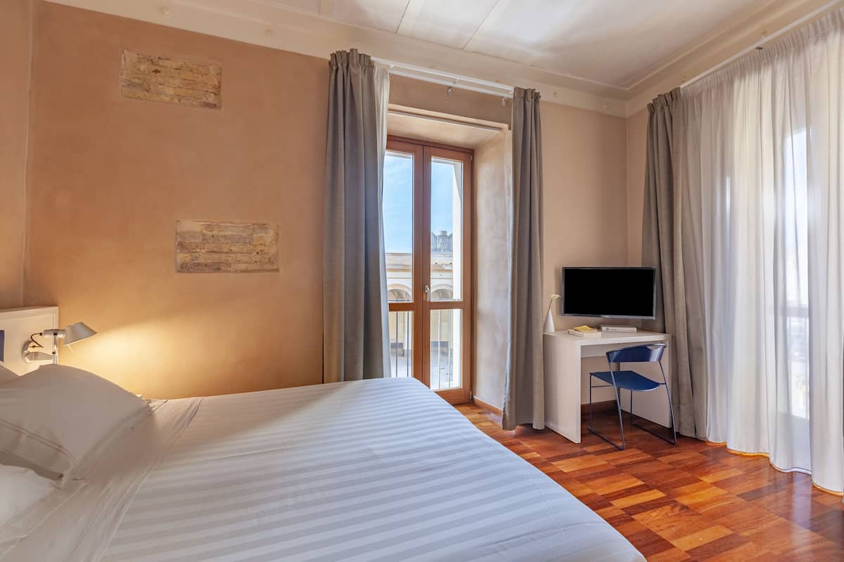 Habitación de hotel con cama, escritorio con silla, televisor y ventana con cortinas.