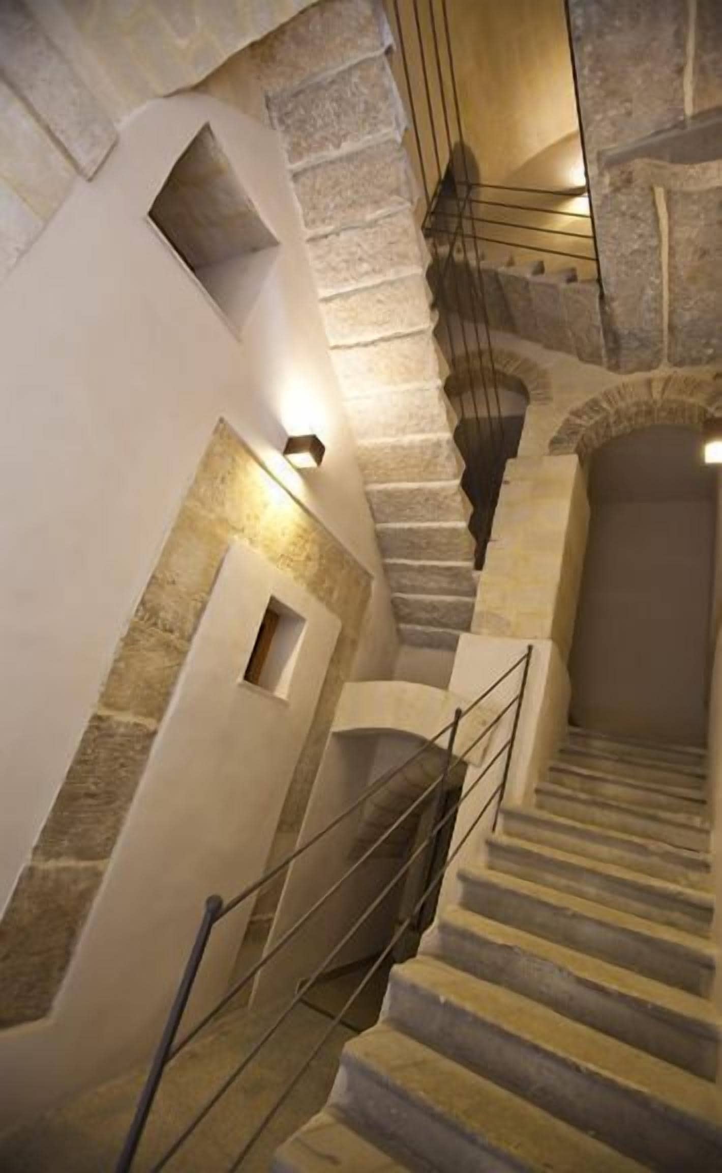 Un escalier en pierre avec une rampe métallique, menant à un niveau supérieur.