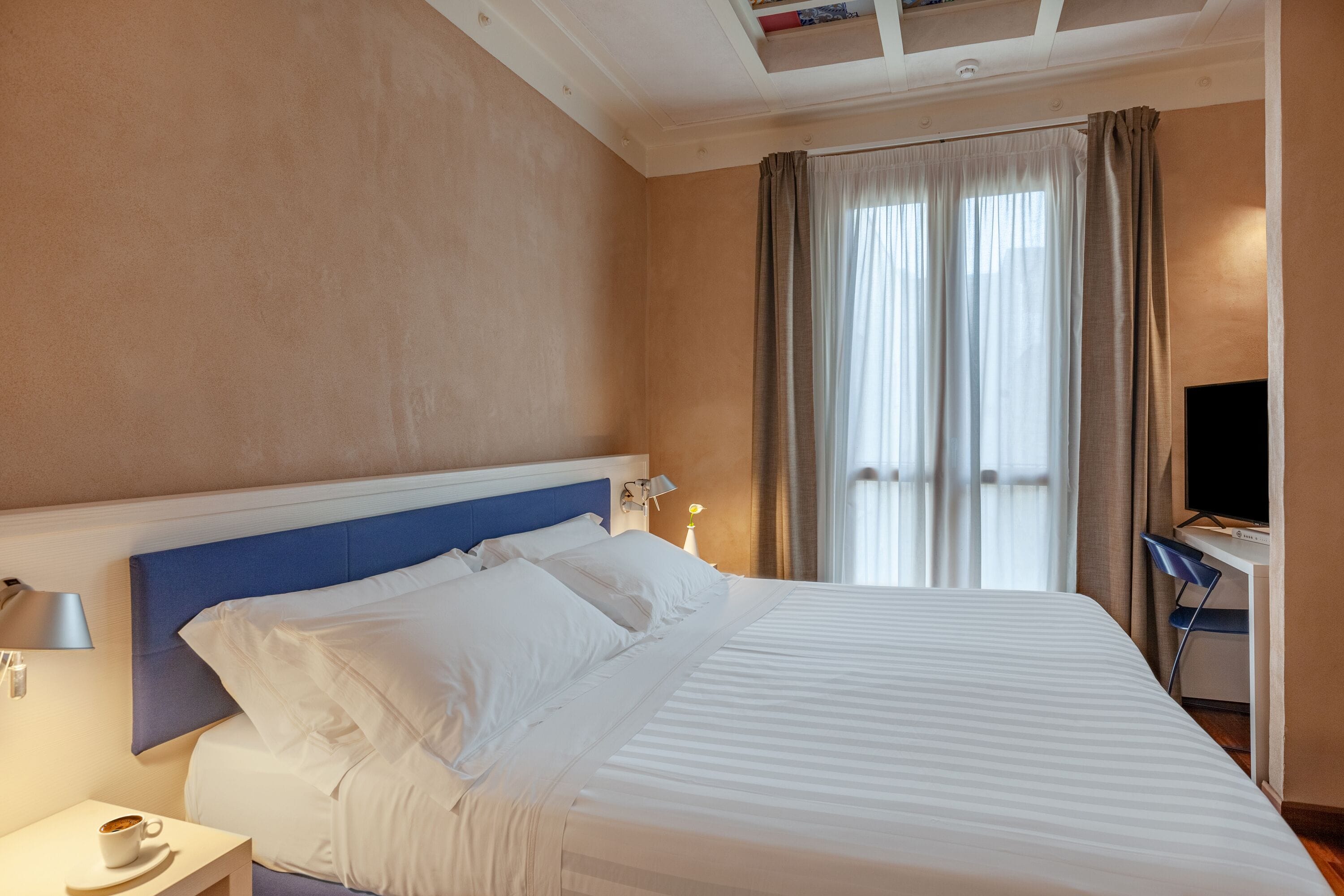 A hotel room with a large bed, a desk with a chair, a television, and a window with curtains.