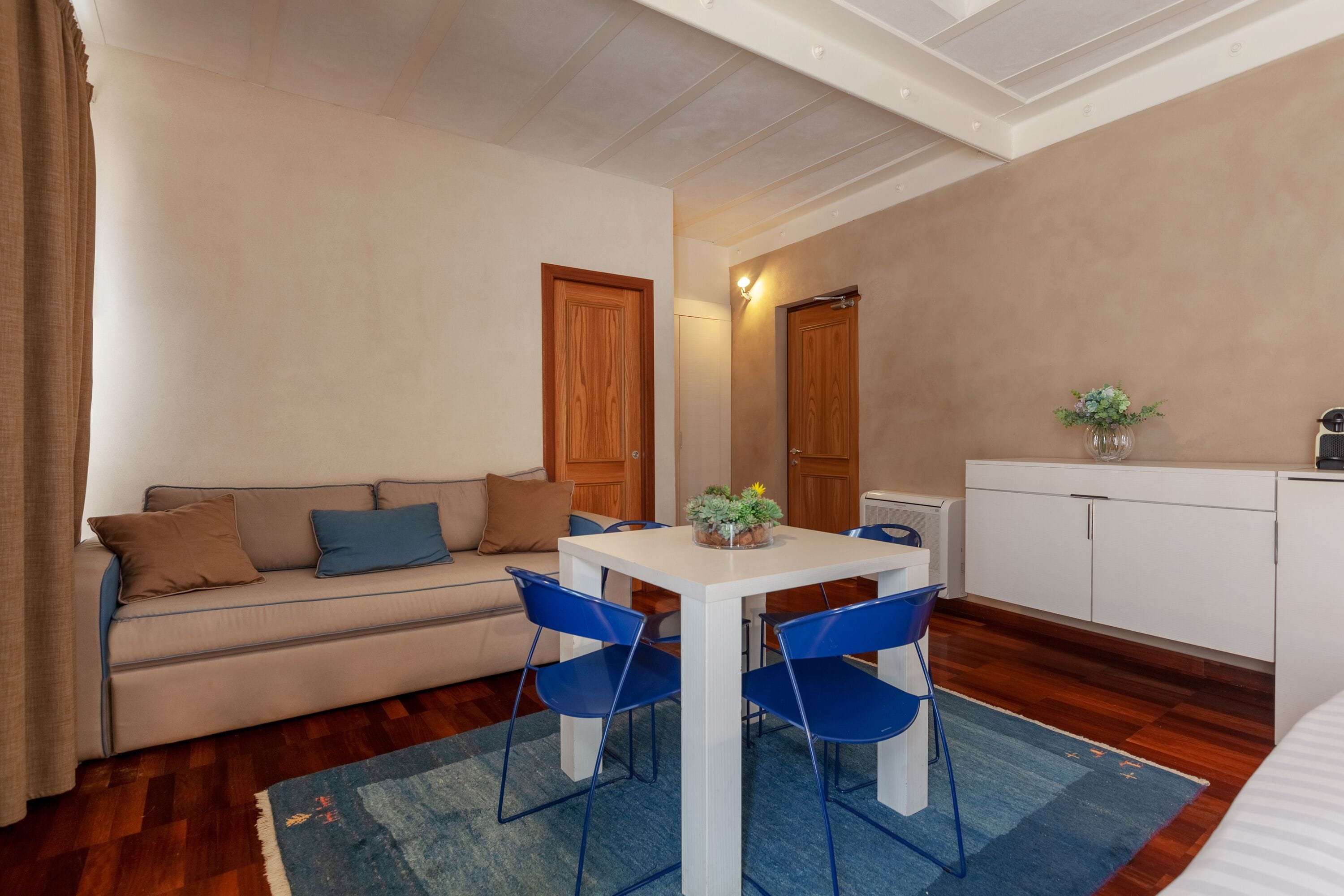 Un espacio habitable compacto con sofá, mesa de comedor con sillas, kitchenette y una planta pequeña sobre la mesa.