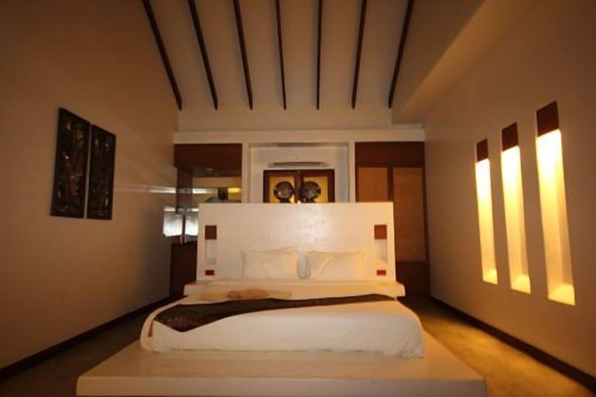Habitación de hotel con una cama grande, techo con listones, puerta con espejo e iluminación en la pared.