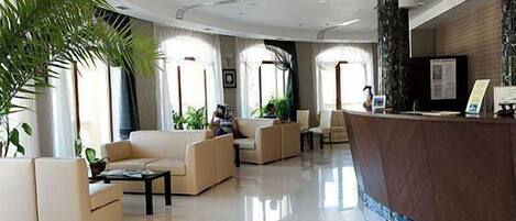 Um hall amplo com balcão de recepção, assentos confortáveis e grandes janelas que permitem a entrada de luz natural.