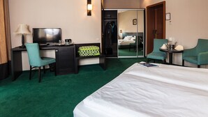 Une chambre d’hôtel comprenant un lit, un bureau avec une télévision, une chaise, une petite table avec une lampe et un miroir.