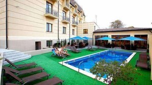 Une piscine entourée d’un bâtiment doté de balcons, avec des chaises longues et des parasols à proximité.