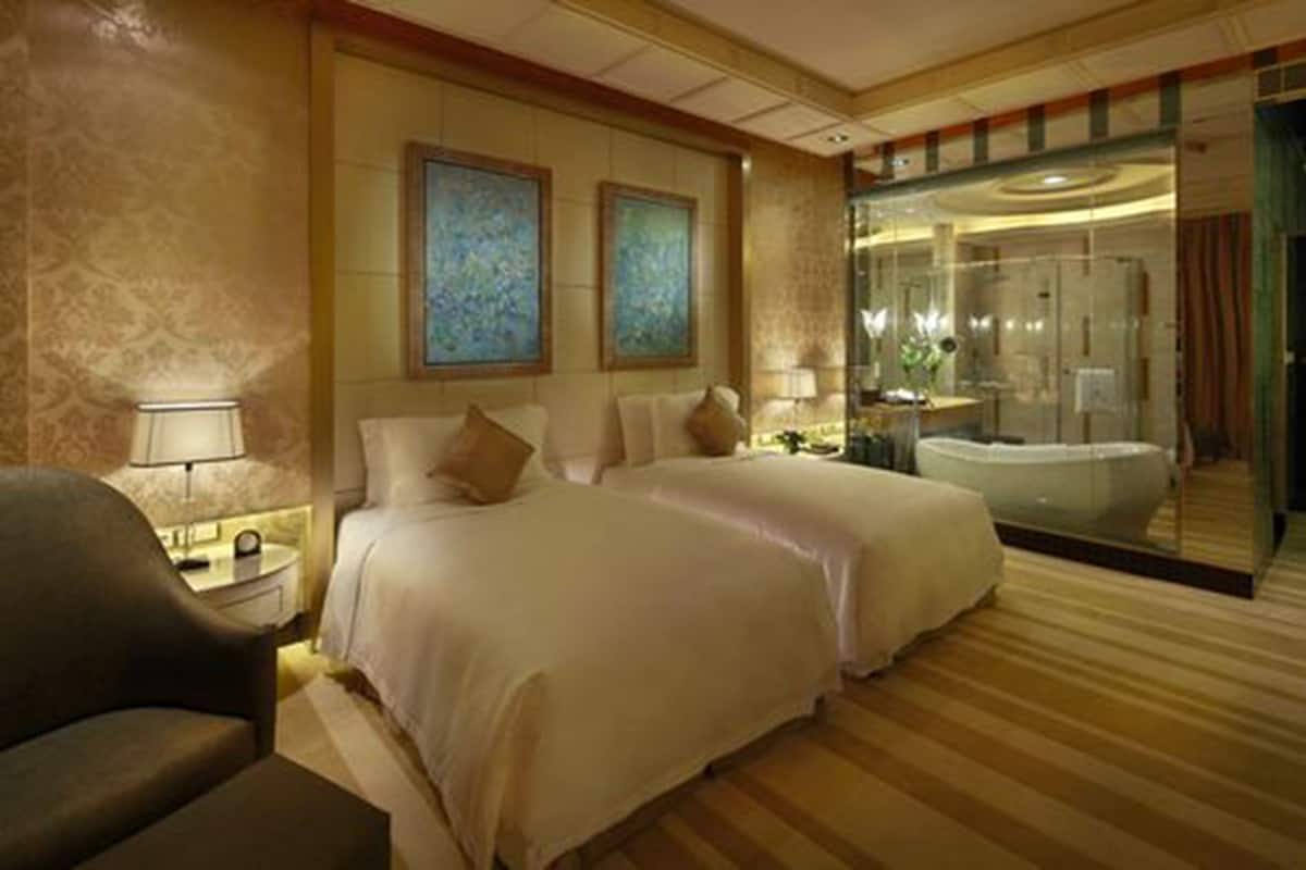 A hotel room with two beds, a sitting area, a large mirror, and a bathtub.