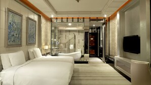 Une chambre d’hôtel avec un grand lit, un coin salon avec un fauteuil, une télévision et un espace douche.