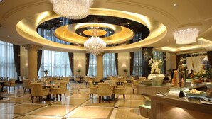 Un hall d’hôtel spacieux, agrémenté d’un grand lustre central, de plusieurs espaces de détente et d’un comptoir de buffet.