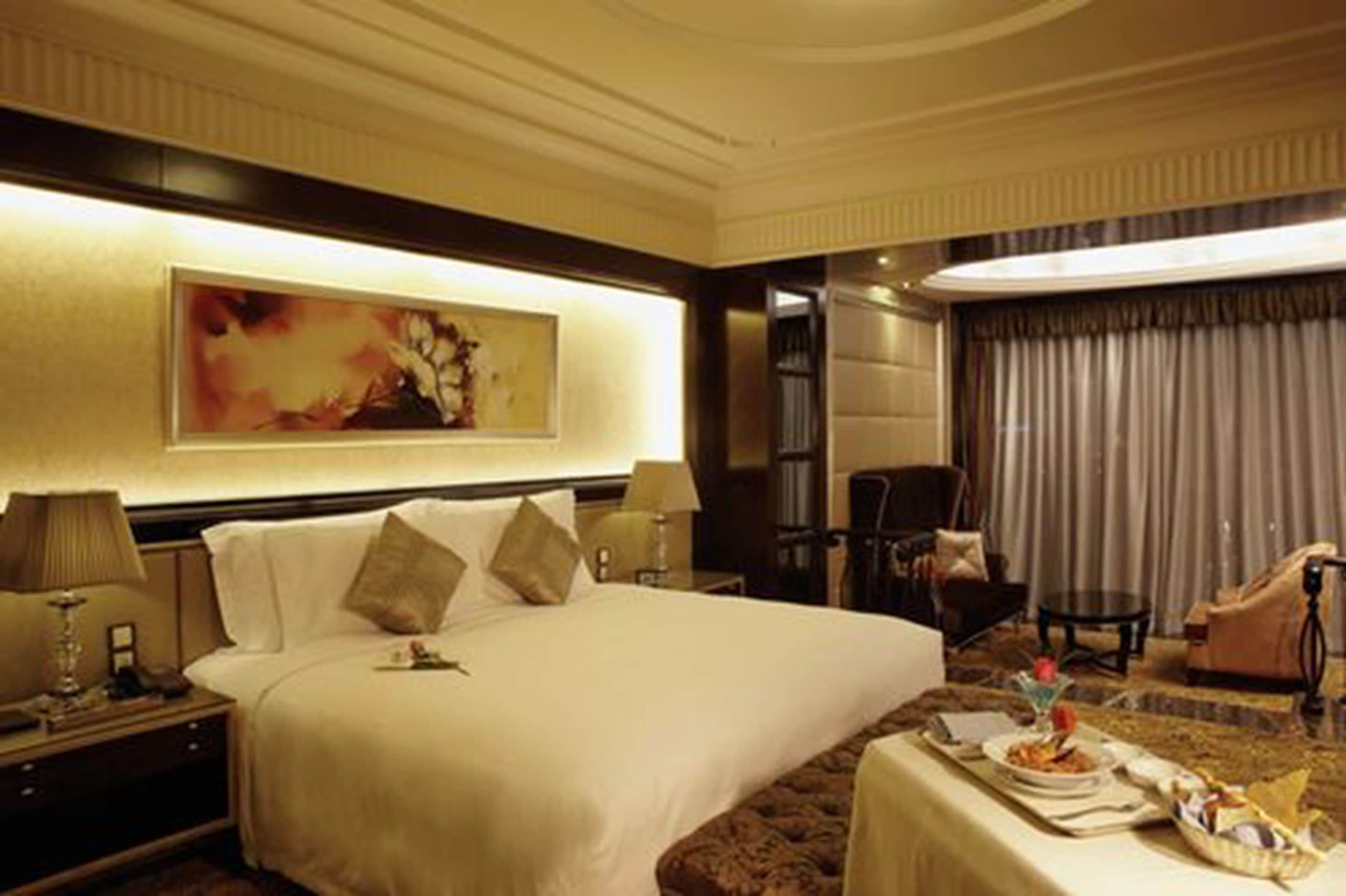 Una habitación de hotel con una cama grande, un cuadro en la pared, un área de comedor con una mesa para dos personas y una silla.