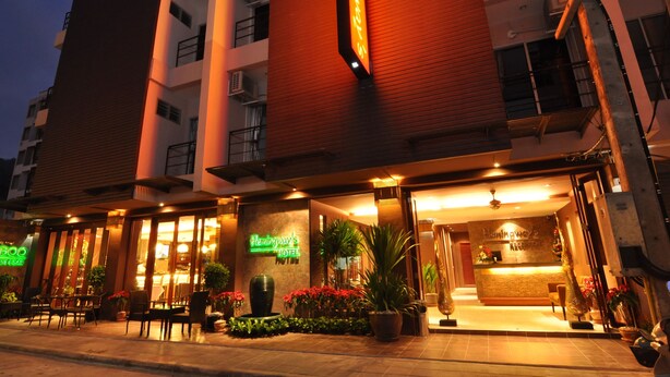 Entrada de hotel con mostrador de recepción, plantas en macetas y asientos exteriores.