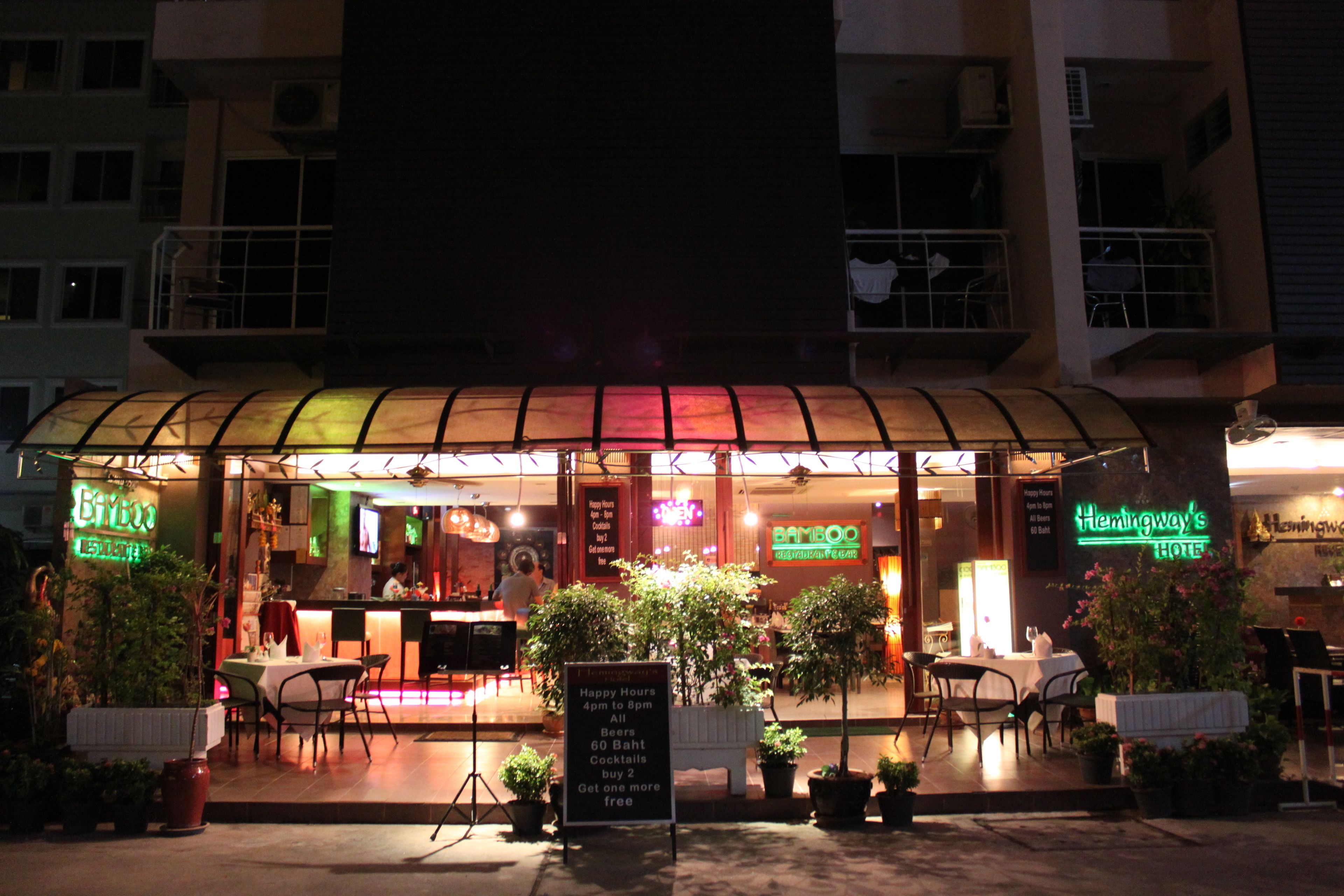 A restaurant with a glass enclosure, outdoor seating, and neon signs.
