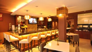 Zona de bar con diferentes opciones de asientos, incluyendo taburetes y mesas, y un televisor montado en la pared.