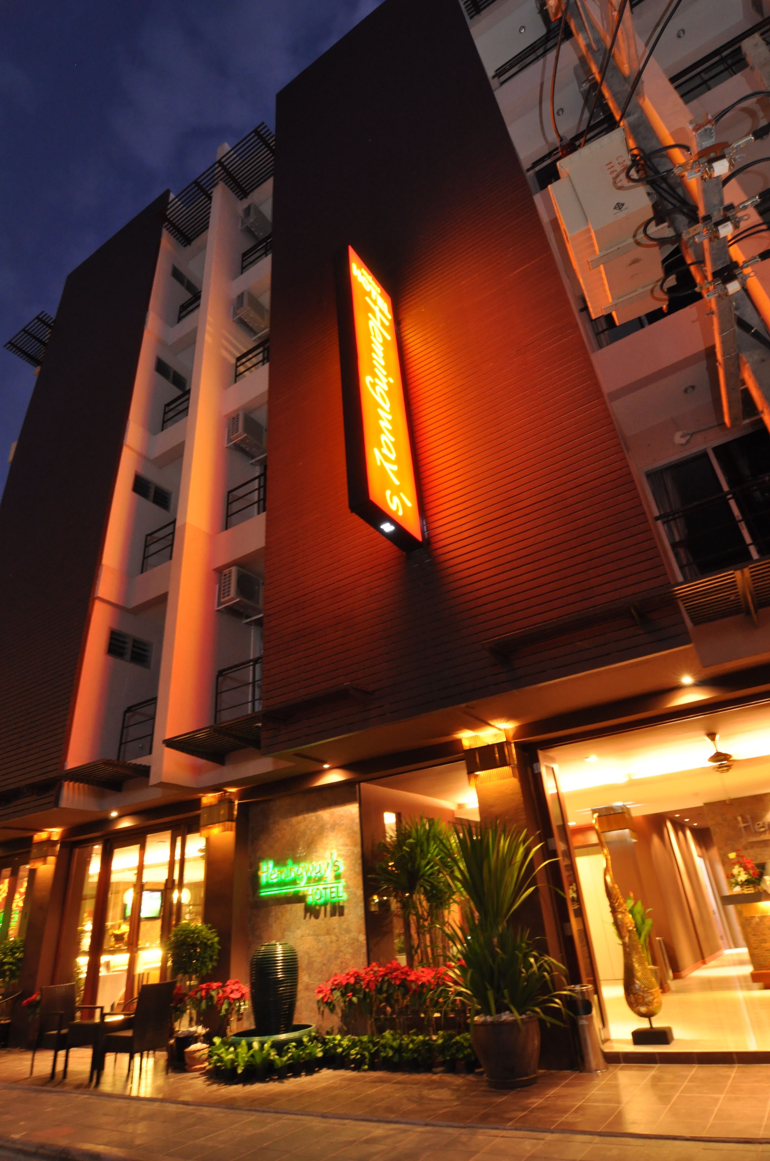 Ein Hotel mit auffälligem Neonlicht, mehreren Etagen und einem gut beleuchteten Eingang mit Blumentöpfen.